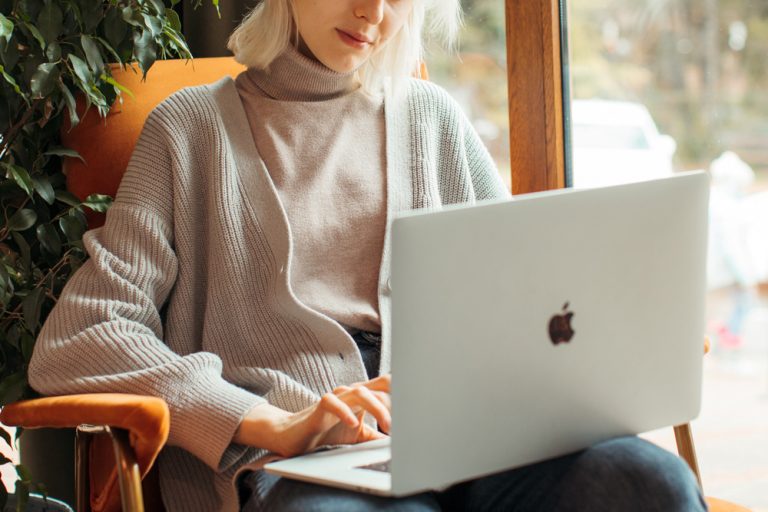 Image of a woman sitting in a chair smiling while typing on a laptop. Work toward healing with the help of online therapy in Parkland, FL.
