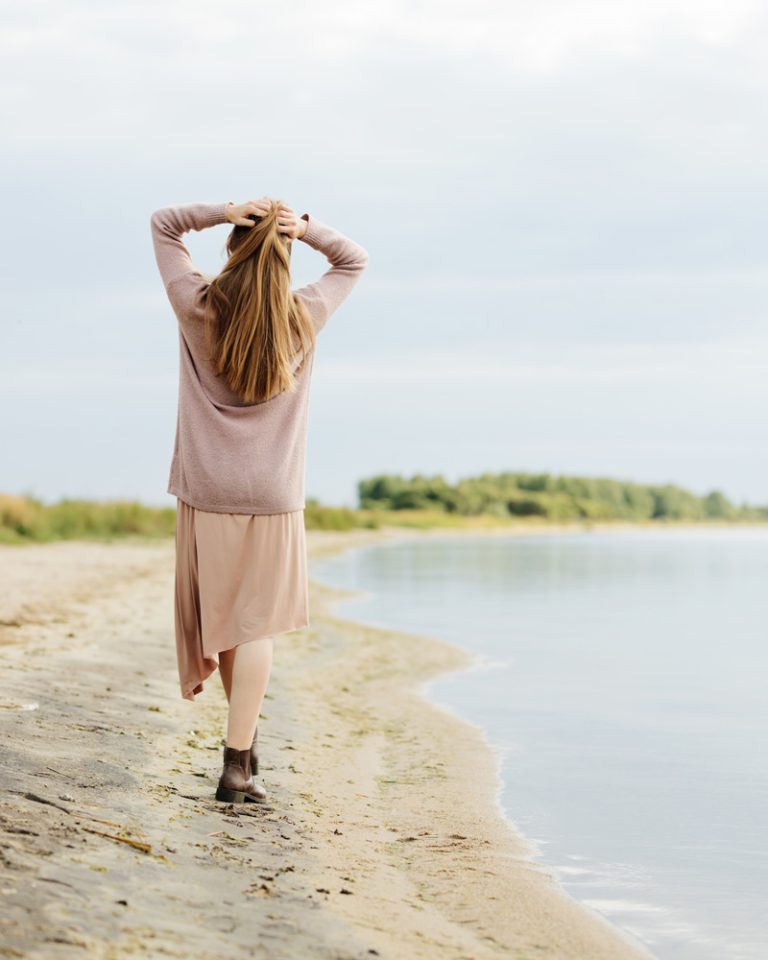 Photo of a woman walking on beach with arms raised and hands on head feeling peace. Discover how Cognitive Behavioral Therapy in Parkland, FL is an effective treatment for anxiety and depression.