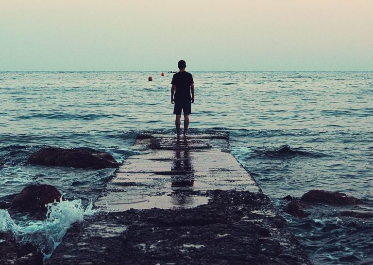 Image of a man standing at the end of a dock, looking at the ocean during twilight. If you struggle with depression, symptoms, learn how CBT therapy in Parkland, FL can help!