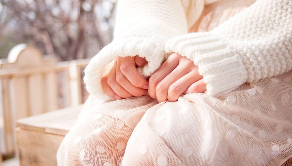 Image of a woman wearing white sitting outside on a bench gripping her dress with her hands anxiously. Learn to overcome your self-esteem issues and depression symptoms with the help of depression counseling in Parkland, FL.