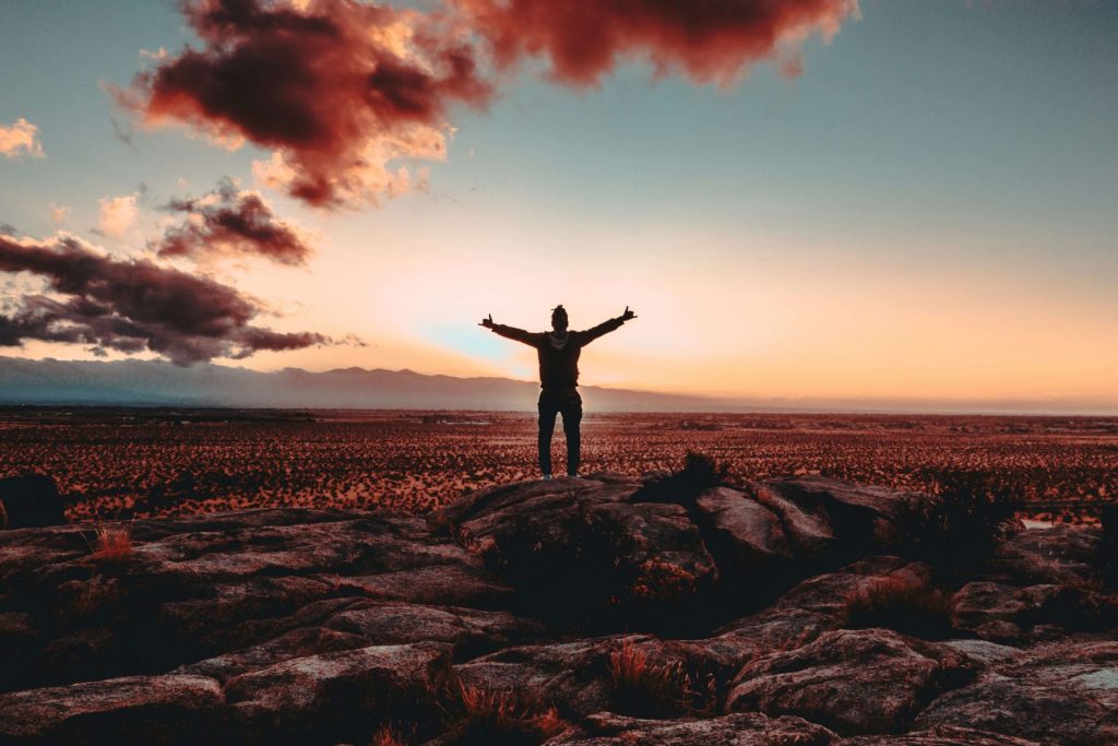 Image of a man standing on top of a mountain with his arms spread open during the sunrise. Manage your depression after a major life change with depression counseling in Parkland, FL.