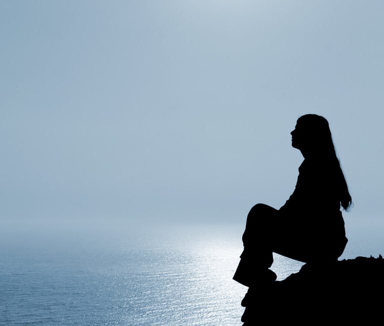 Image of a meditating woman sitting on a rock by the ocean. Discover how depression counseling in Parkland, FL can help you overcome your depression symptoms in positive ways.