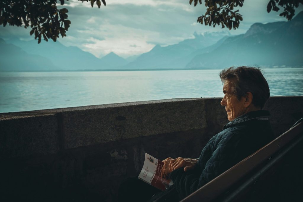 book | depression counseling in parkland, fl | depression therapist in parkland, fl | major life changes | major life changes and depression | signs of depression | 33073 | 33067 | 33076 Image of a man sitting outside on a bench holding a book while looking out at a lake surrounded by mountains. Learn effective ways to cope after major life changes with the help of a skilled depression therapist in Parkland, FL.