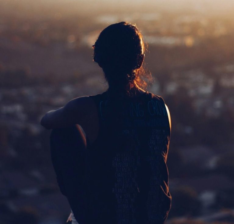 Image of a woman sitting on top of a hill overlooking a city skyline. If you are going through a major life change, work with a depression therapist to help you cope with the changes. With depression counseling in Parkland, FL you can find support.