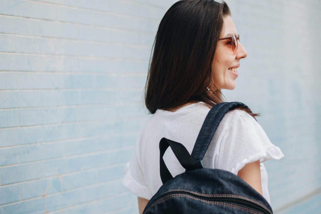 woman smiling | anxiety therapy in coconut creek, fl | anxiety therapist in coconut creek, fl | depression counseling | signs of depression | college student anxiety | 33063 | 33066 | 33073 Image of a smiling woman standing outside wearing sunglasses and a backpack. This image represents the feeling of happiness after tackling college student anxiety with the help of anxiety therapy in Coconut Creek, FL.