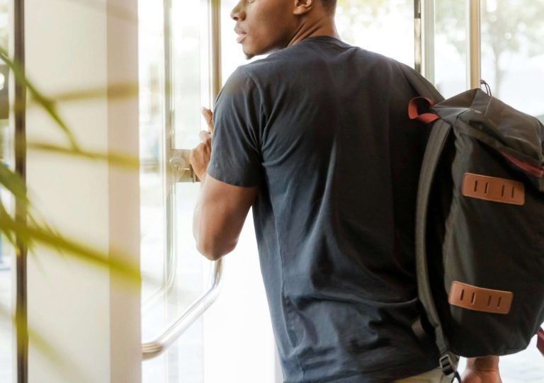 Image of an African American man holding a backpack walking through a door. If you struggle with stress and anxiety as a college student, learn how anxiety therapy in Coconut Creek, FL can help.