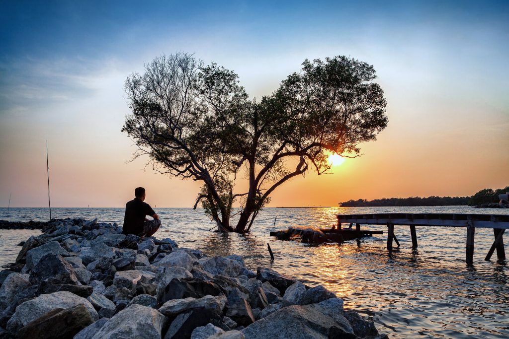 man on rocks | depression counseling in parkland, fl | depression therapist in parkland, fl | high functioning depression | cbt for depression | signs of depression | 33073 | 33067 | 33076 Image of a man sitting on rocks looking at the ocean during sunset. Find relief from your high functioning depression with the help of depression counseling in Parkland, FL.